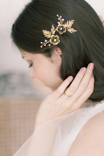 Woman with dark hair wearing a gold floral hair clip with leaves and small bead accents.