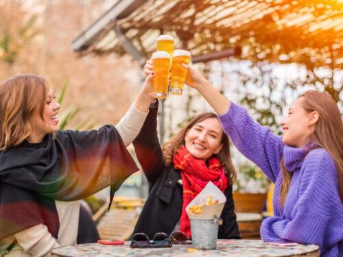 Women clinking glasses of beer in a cozy brewery—one of the fun winter bridal shower venues.
