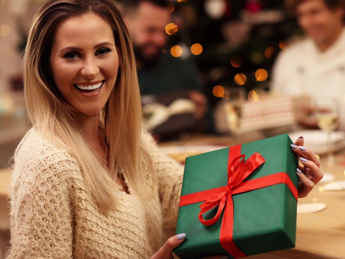 Christmas gifts for bride-to-be featured image showing a woman exchanging christmas gifts with friends.